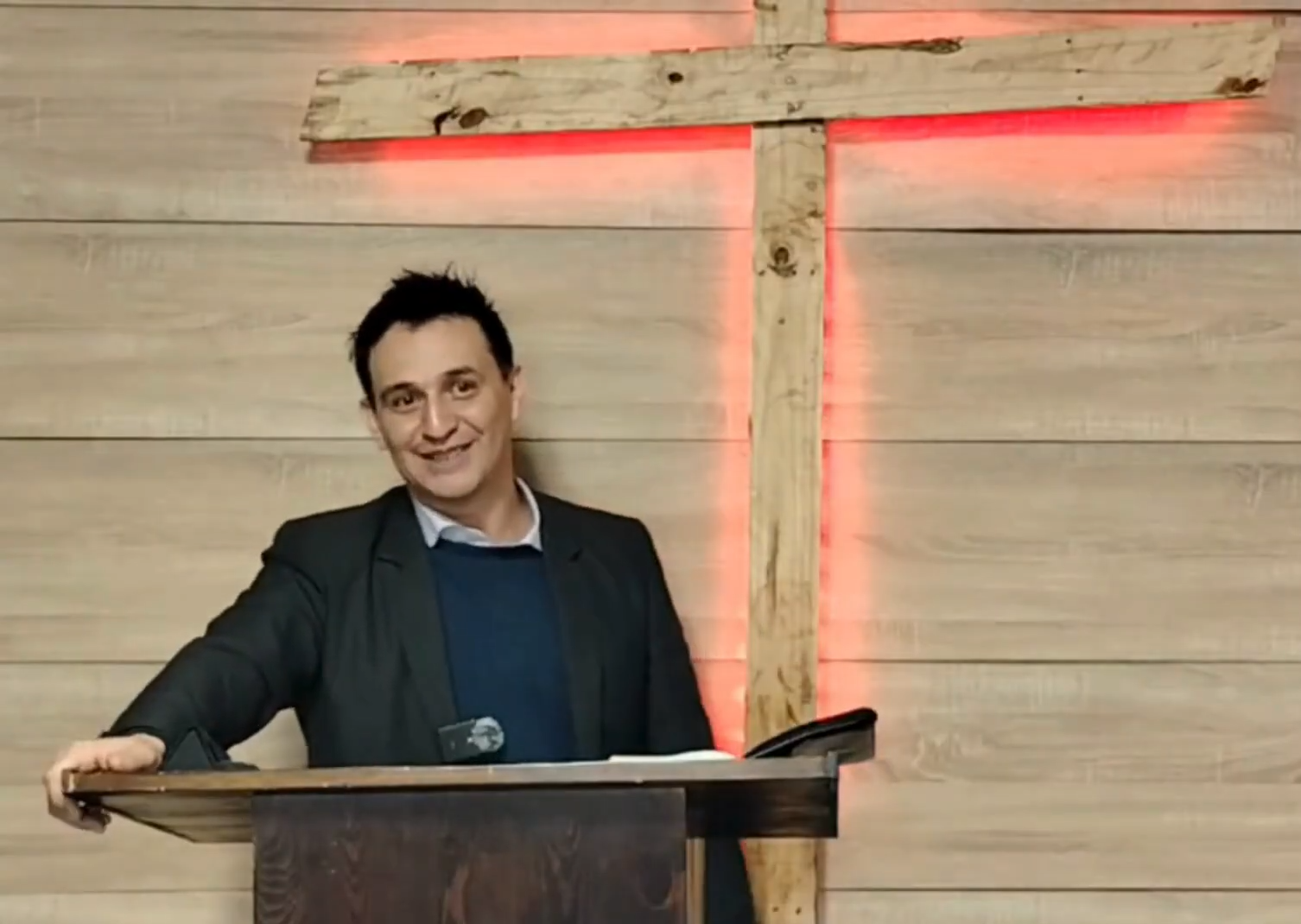 Pastor Maikol Cabrera predicando desde el púlpito, con una cruz de madera detrás